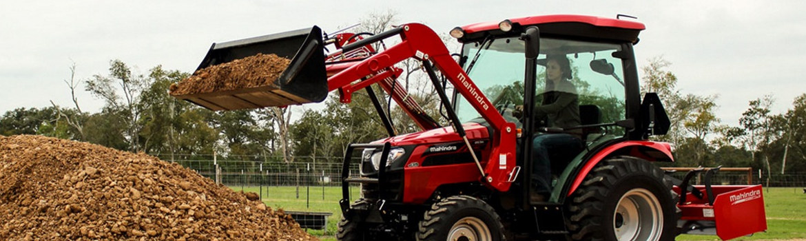 Woman in a Mahindra 2538 4WD HST cab tractor dumping gravel into a pile on a farm