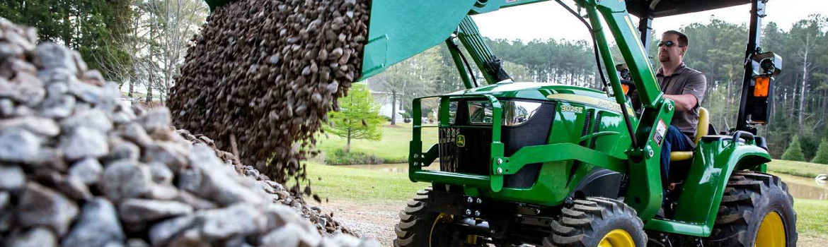 Man in a John Deere® 3025E tractor dumping gravel into a pile